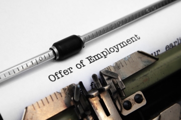 A piece of paper in a typewriter with the words Offer of Employment typed in black ink