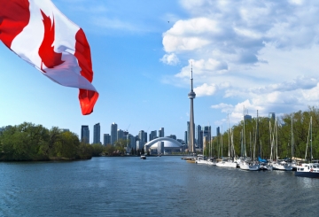 A Canadian flag flutters over a lake, with a view of Toronto in the background