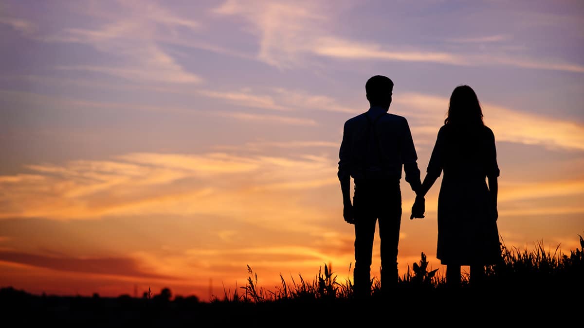 A couple holding hands under the sunset.