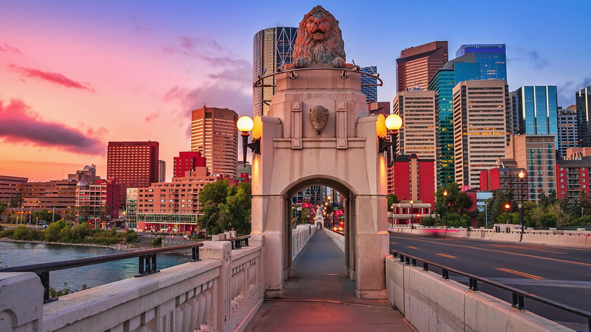 A scenic view of a walkway leading towards downtown Calgary under a colorful sunrise sky.