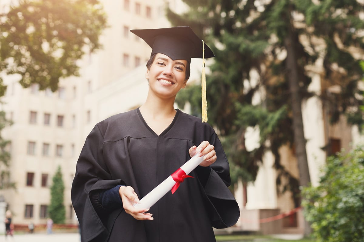 Graduate holding diploma in hand, facing camera