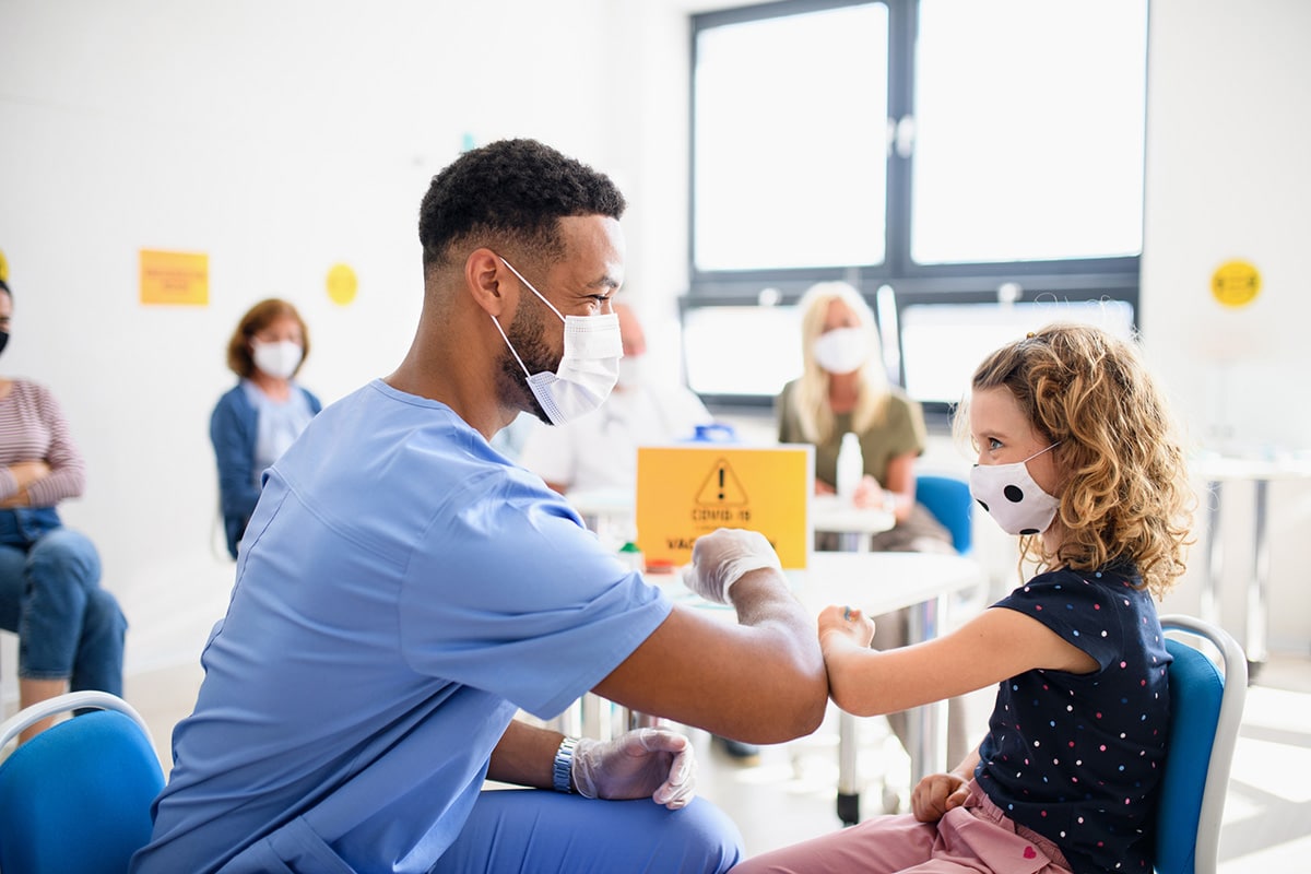 Healthcare worker wearing surgical masks bumps elbows with young patient, also wearing a surgical mask