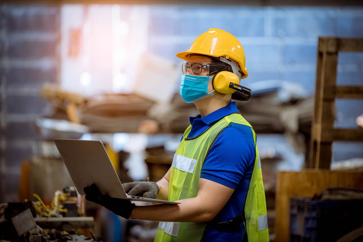 Worker holding a laptop, wearing safety equipment