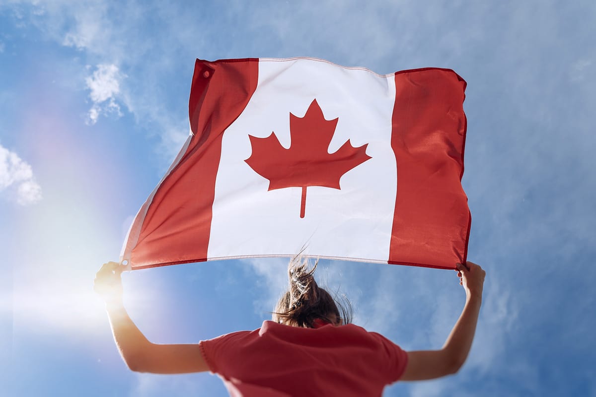 Girl holding Canadian flag under blue sky.