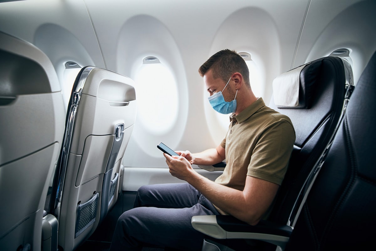 Man checking cellphone on airport, wearing surgical mask