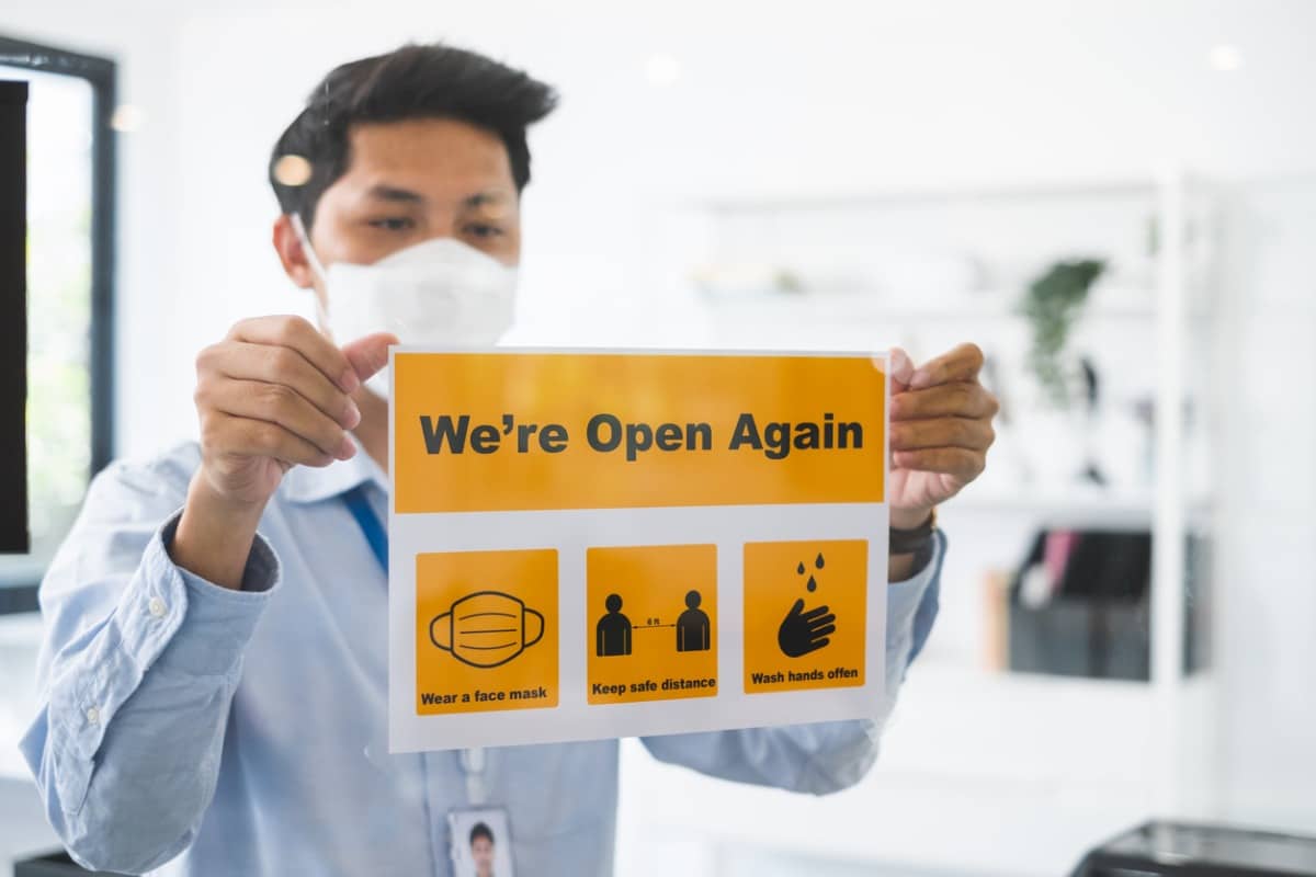 Business owner putting up "open" sign with COVID-19 safety warnings.