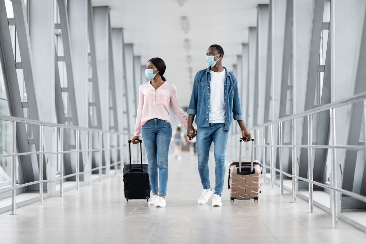 Travellers walking through an airport with luggage, wearing surgical masks