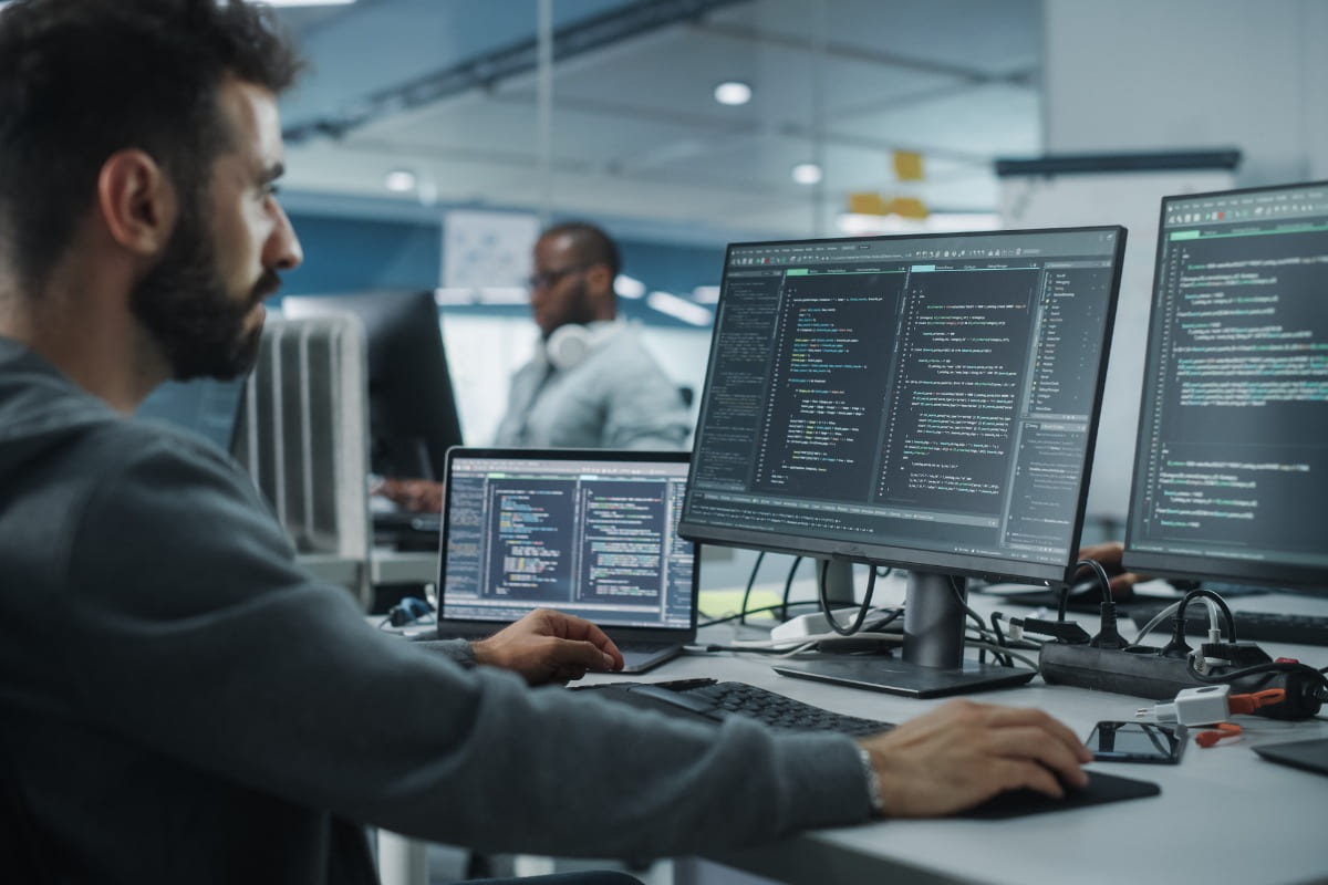 man working in tech job looking at two computer monitors