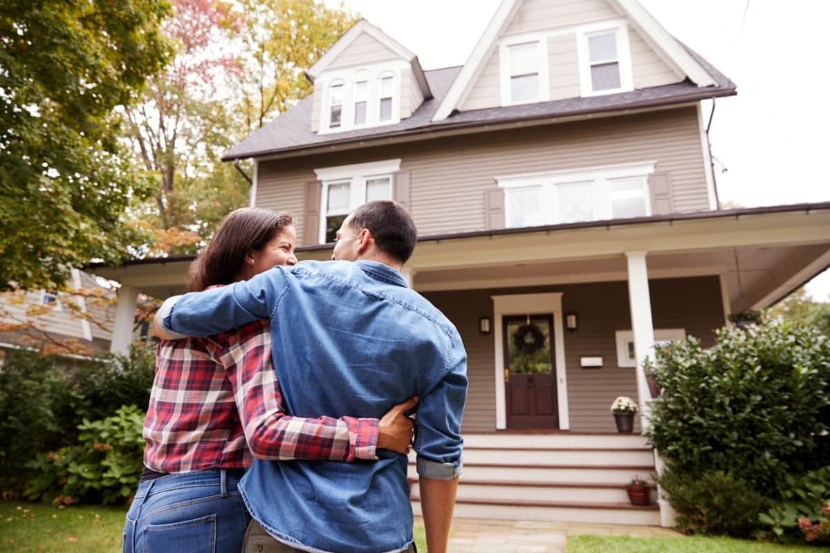 couple looking at eachother smiling in front of a new home
