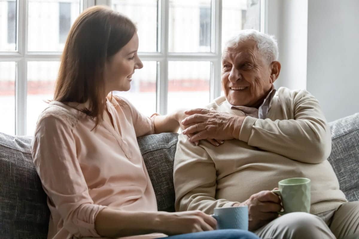 young woman smiling at elderly man sitting on a couch