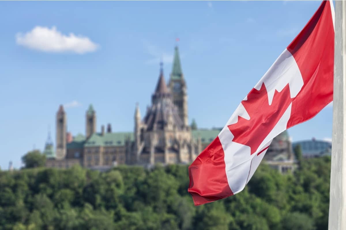 Canadian flag in foreground wit building and forest behind it