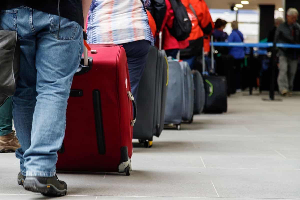 Group of people with luggage lining up at an airport check-in counter