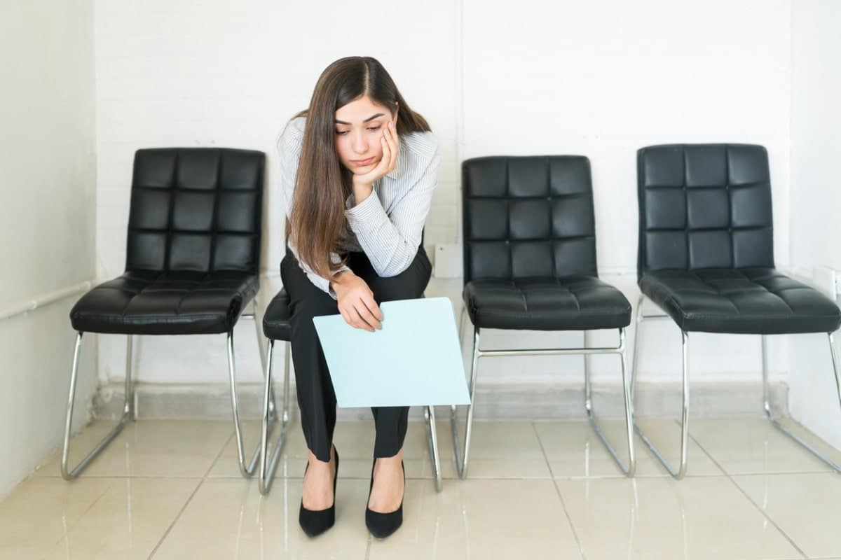 woman sitting in a chair with her head down. She looks unhappy, as she holds a piece of aper in her hand.