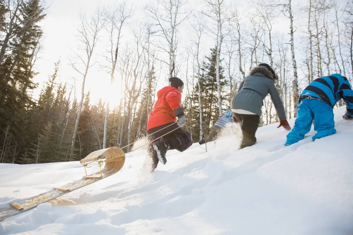 Family walking up snowy hill pulling toboggan