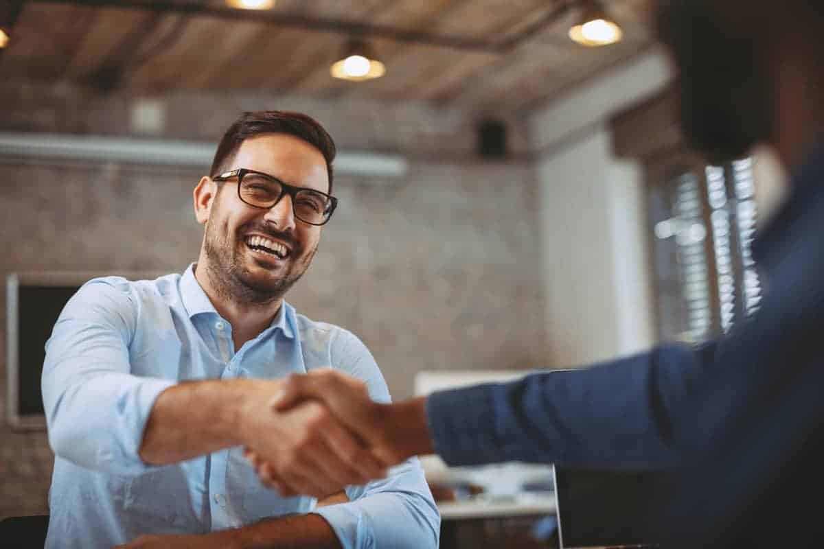 A man being hired for a job, shaking hands with the interviewer. Canada is experiencing record low unemployment as of January 2023.
