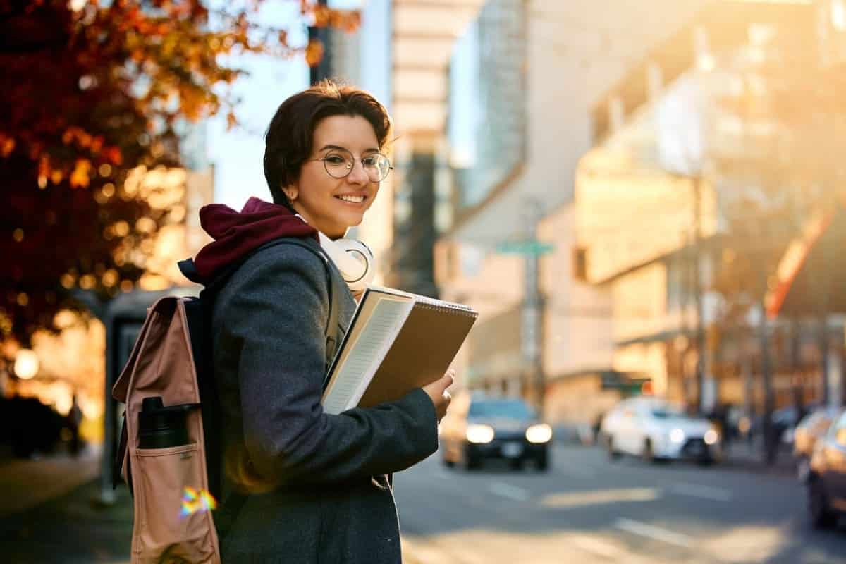 Young happy female student standing on the street and looking at camera