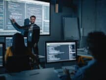 Teacher Giving Computer Science Lecture to Students in Dark College Room, projecting Slideshow with Programming Code.