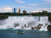 The Maid of the Mist cruise tour boat in front of The American and Bridal veil falls with tourists on the top of the boat and along the edge