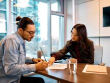 Two people sitting at a desk in an office building.