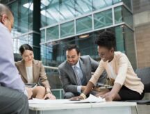 A group of professionals sit at a low-table discussing business plans.