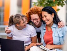 A diverse group of cheerful female college students sitting in front of a university building, talking, smiling