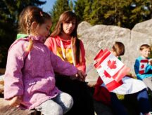 Family of mother with three kids hold large Canadian flag celebration in mountains