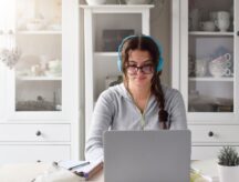student in headphones sitting at a desk studying at home in front of laptop computer