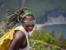 A young lady smiles at the camera with a lake in the background.