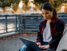 Young woman surfing the net on laptop in the park.