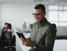 A young man smiling in an office building while looking at his phone.