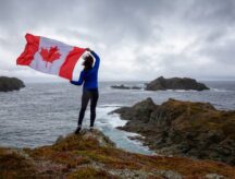 A woman holds a Canadian flag while standing close to a picturesque waterbody