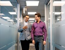 Two young businessmen walking through an office building while being work permit-exempt.