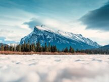 A mighty mountain stares back at the camera as snow decorates the foreground of the image.
