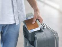 A man's hand holding a passport, a map and a suitcase.
