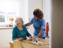 A home care worker attends to a patient in a well lit room.