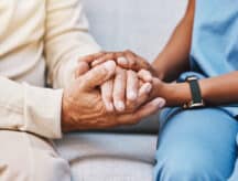 A closeup of the hands of a caregiver and the hands of the care receiver on a couch.