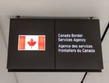 A Canadian flag next to a bilingual sign reading Canada Border Services Agency located in Terminal 3 of Toronto Pearson airport. Often referred as the CBSA, Canada Border Services Agency is the law enforcement agency tasked with protection of all Canadian border access.