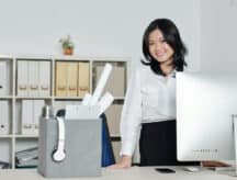 A young woman in corporate clothing smiles while in an office