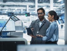 Indian Male Industrial Engineer And Hispanic Female Supervisor Using Laptop And Talking At Electronics Factory