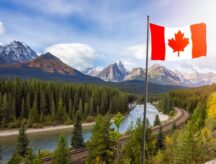 The Canadian flag hoisted atop a flagpole in the foreground, with Banff National Park in the background.