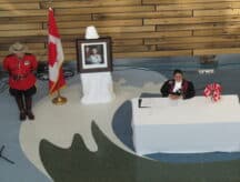 A citizenship judge presiding over a citizenship Ceremony (located in Toronto), with a portrait of Queen Elizabeth II, a Canadian flag, and a Royal Canadian mounted Police officer behind her.