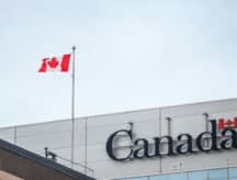 The Canadian flag atop a Government of Canada building with the official Canada watermark.