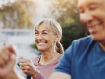 A middle-aged lady smiling joyously with a middle-aged man partially out of frame on the right (blurred).