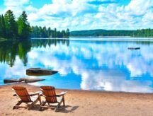 Two beach chairs at the shore of a lake, on a bright summer day.
