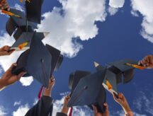 A group of graduates about the throw their caps into a blue sky.