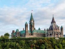Parliament Hill in Ottawa, Ontario on a cloudy day, with some greenery visible.