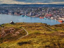 A view of the St. John's city skyline and harbour on a semi-cloudy day, with grassy fields in the forefront.