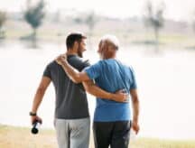 A picture of a son and elderly father on a walk together near the lake.