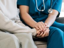 A caregiver and their elderly charge holding hands.