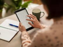 Woman sitting at a table holding a tablet which she is using to look at a calendar.
